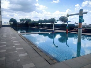 Una piscina con plataforma de baldosas, sillas de descanso y cielo despejado.