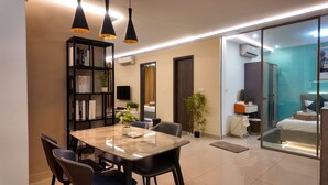 A modern hotel room with a dining area, a bookshelf, a mirror, and a sliding door leading to a balcony. - The Peak Residence by Torent Property (Phnom Penh)