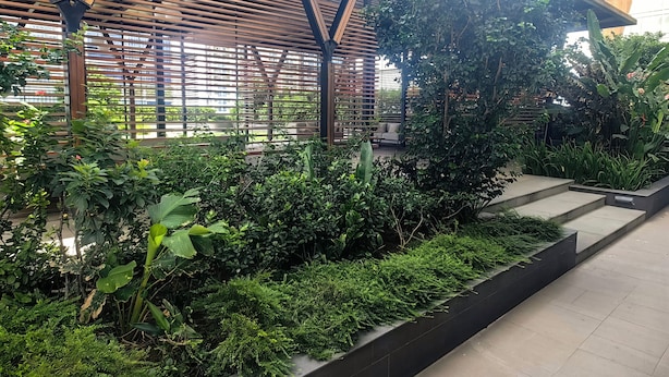 A covered outdoor area with a wooden structure, lush greenery, and a concrete pathway. - The Peak Residence by Torent Property (Phnom Penh)