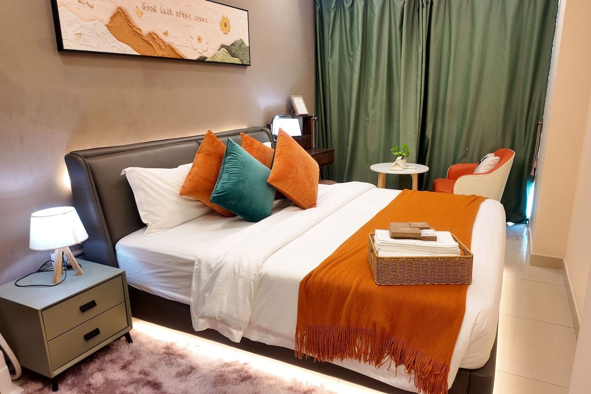 Habitación de hotel ordenada con cama, mesita de noche, lámpara y una pequeña mesa con una planta.