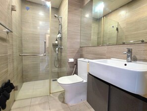 Un baño moderno con cabina de ducha de vidrio, inodoro blanco y un lavamanos grande con espejo superior.