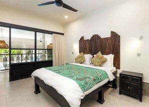 A bedroom with a bed, a nightstand, a ceiling fan, and a window with a view. - Villa Baruna Seminyak (Seminyak)