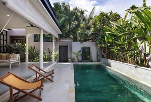 A pool area with lounge chairs, a covered seating area, and lush tropical plants. - Villa Baruna Seminyak (Seminyak)