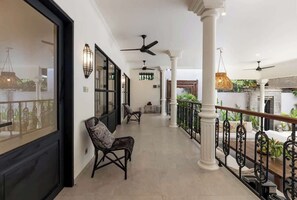 A covered corridor with ceiling fans, a bench, and a railing with potted plants. - 3BDR Villa Baruna, Good Location (Seminyak)