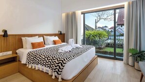 Habitació d'hotel moderna amb un llit gran, una taula de nit, una finestra amb cortines i vista a vegetació exterior.