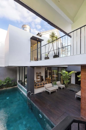 Ein modernes, zweistöckiges Haus mit Pool, Außenbereich und einem Balkon mit Pflanzen.