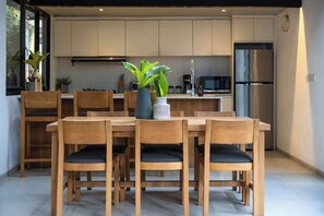 Eine moderne Küche mit Holzausbau, einem Edelstahlkühlschrank und einer Essecke mit Holzbeschlägen und einem zentralen Tisch.