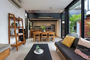 Ein modernes Wohnzimmer mit Sofa, Couchtisch und Bücherregal, das in eine Küche und einen Essbereich übergeht.