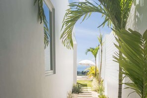 A narrow pathway leading to a white building with a view of the ocean. - Villa Lola with Ocean View & Breakfast (Uluwatu)