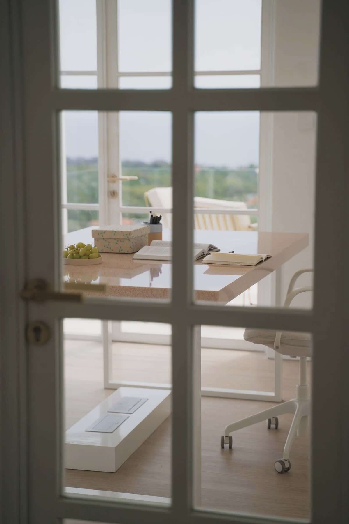 Blick durch eine Tür auf einen Balkon mit Tisch, Stuhl und Wagen.