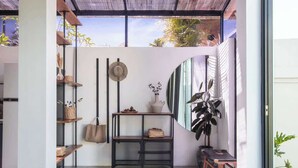 Ein modernes Interieur mit Glastrennwand, Regalen mit Körben, einem Hut, einer Vase mit Blumen und einer großen Pflanze.