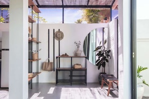 Ein modernes Interieur mit Glastrennwand, Regalen mit Körben, einem Hut, einer Vase mit Blumen und einer großen Pflanze.