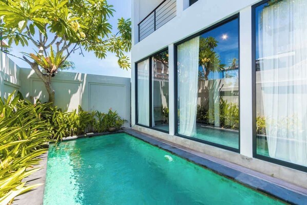 Ein modernes Haus mit Swimmingpool, großen Fenstern und üppiger Bepflanzung.
