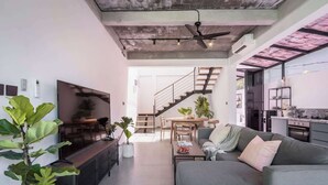 Ein modernes Wohnzimmer mit einem grauen Sofa, einem Fernseher und einer Treppe zu einem Küchenbereich.