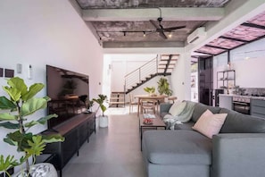 Ein modernes Wohnzimmer mit einem grauen Sofa, einem Fernseher und einer Treppe zu einem Küchenbereich.