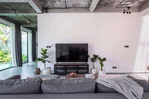 Ein modernes Wohnzimmer mit großem Flachbildfernseher, grauen Sofas und Topfpflanzen.