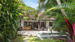 A modern house with a pool, surrounded by lush greenery and a patio with outdoor furniture.