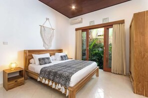 Een slaapkamer met een houten bed, een nachtkastje, een wanddecoratie van macramé en een schuifdeur naar een tuin.