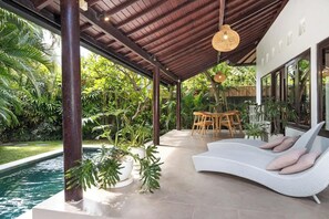 Un espace extérieur abrité, doté d’une piscine, de chaises longues et d’une table à manger, le tout entouré d’une végétation luxuriante.