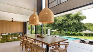 Ein moderner Essbereich mit Holztisch und Stühlen, großen Fenstern und Blick auf einen Pool und Grünflächen.