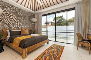 A bedroom with a bed, a window, a chair, and a patterned wall. - PianoPiano Villas in Uluwatu. Breakfast included! (Pecatu)