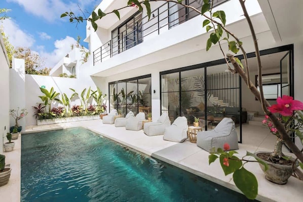 Ein modernes Haus mit Swimmingpool, Sitzgelegenheit im Freien und Topfpflanzen.