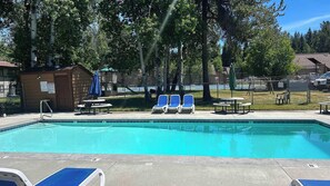Ein Swimmingpool mit Liegestühlen und Tischen, umgeben von Bäumen und einem eingezäunten Bereich.