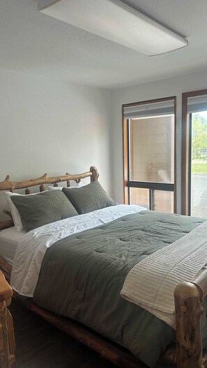 Ein Bett mit hölzernem Kopfteil, ein Fenster mit Ausblick und eine Deckenleuchte.