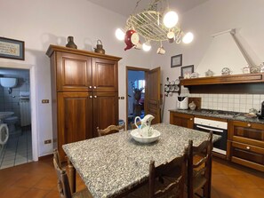 A kitchen with wooden cabinets, a granite countertop, a dining table with chairs, and a hanging light fixture. - Lucia e Francesco by Interhome (Volterra)