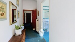 En hall med en träbänk, krukväxter, inramade tavlor på väggen, ett element och ett badrum som syns genom en öppen dörr.