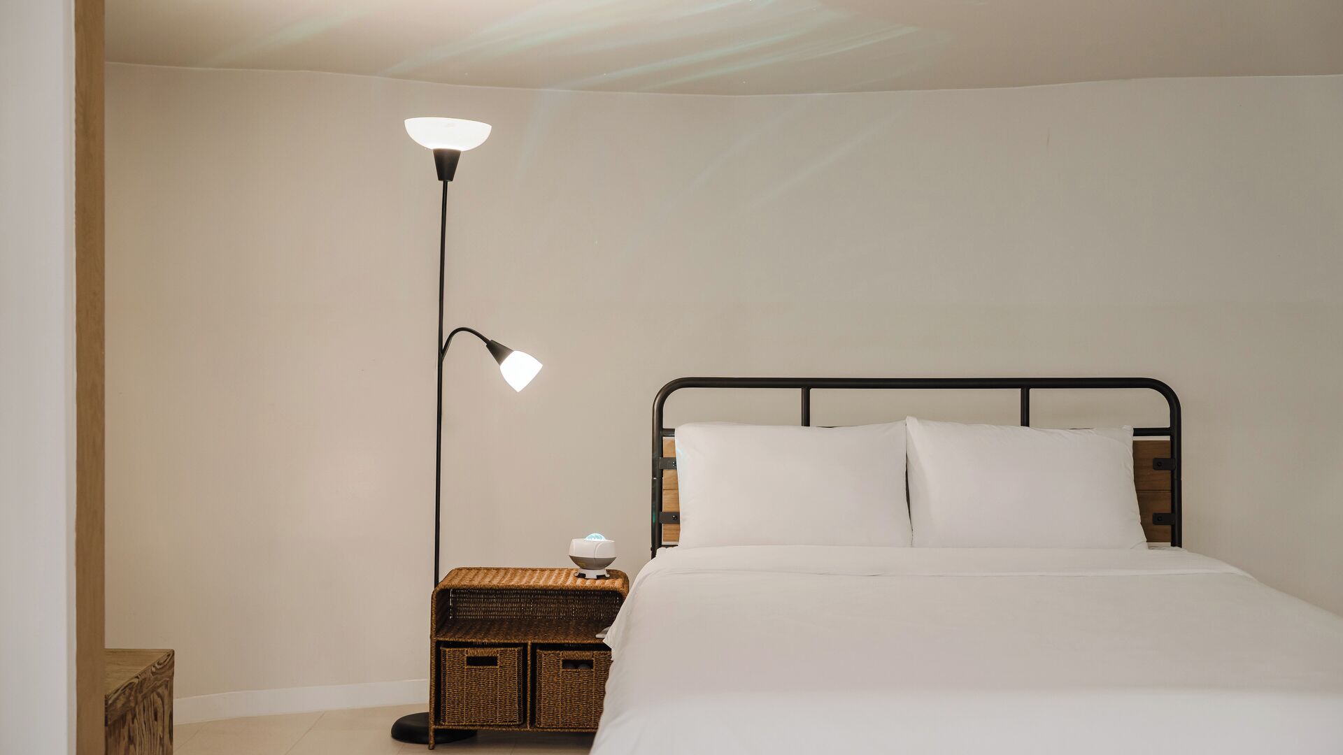 A bedroom with a bed, a nightstand, a floor lamp, and a small wicker basket.