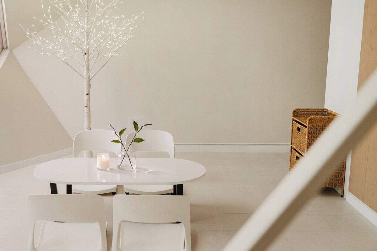 Un comedor minimalista con una mesa redonda, dos sillas, una vela y una rama decorativa.