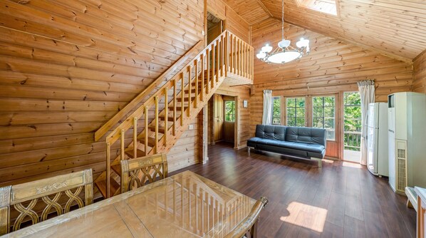 Interior de una cabaña de madera con escalera, sofá, mesa de comedor y refrigerador.