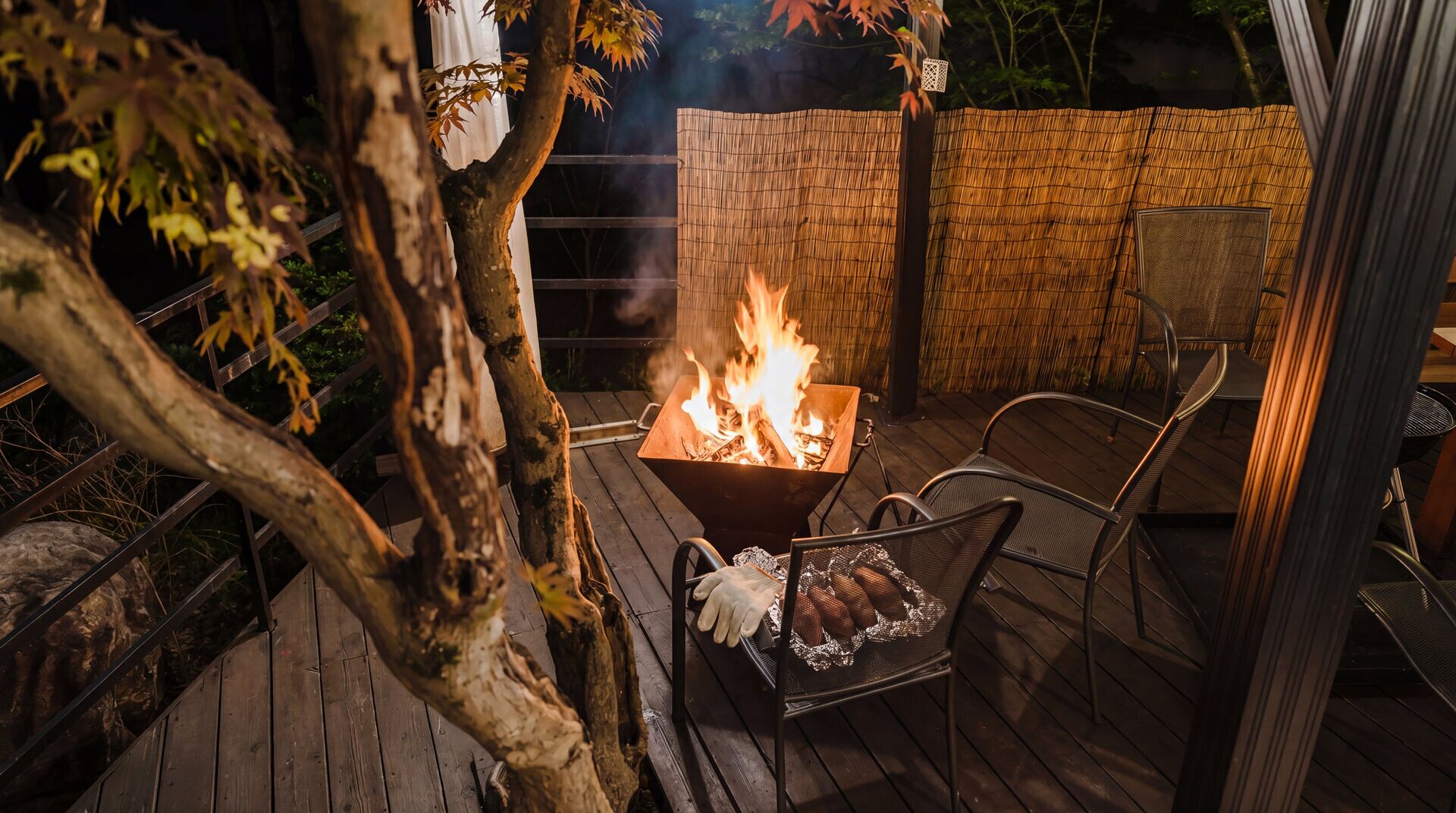 An outdoor patio with a metal grill, a fire pit, and a bamboo fence.