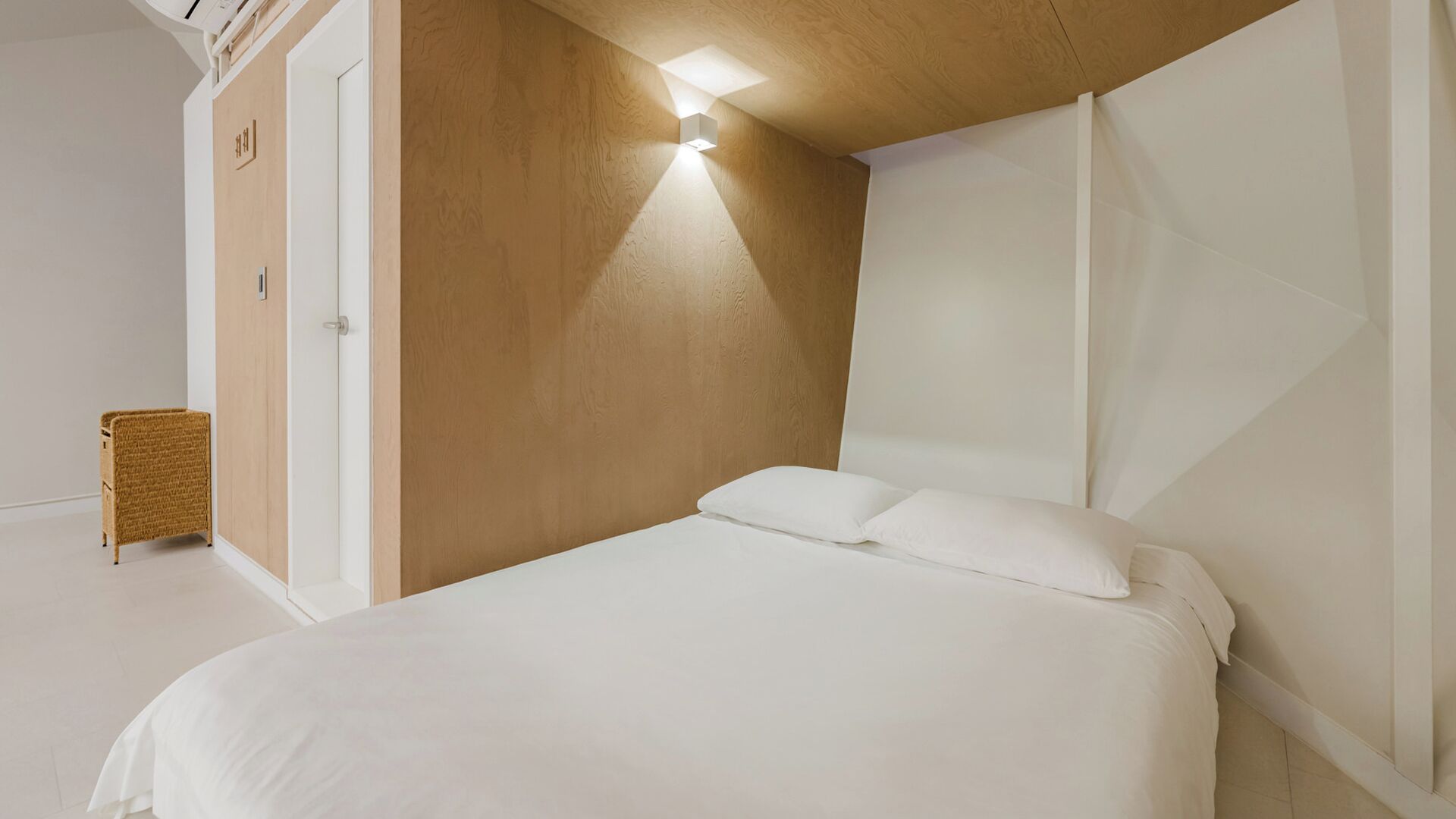 Un dormitorio con cama, pared decorativa de madera, lámpara de pared y mesita de mimbre.