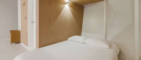 Un dormitorio con cama, pared decorativa de madera, lámpara de pared y mesita de mimbre.