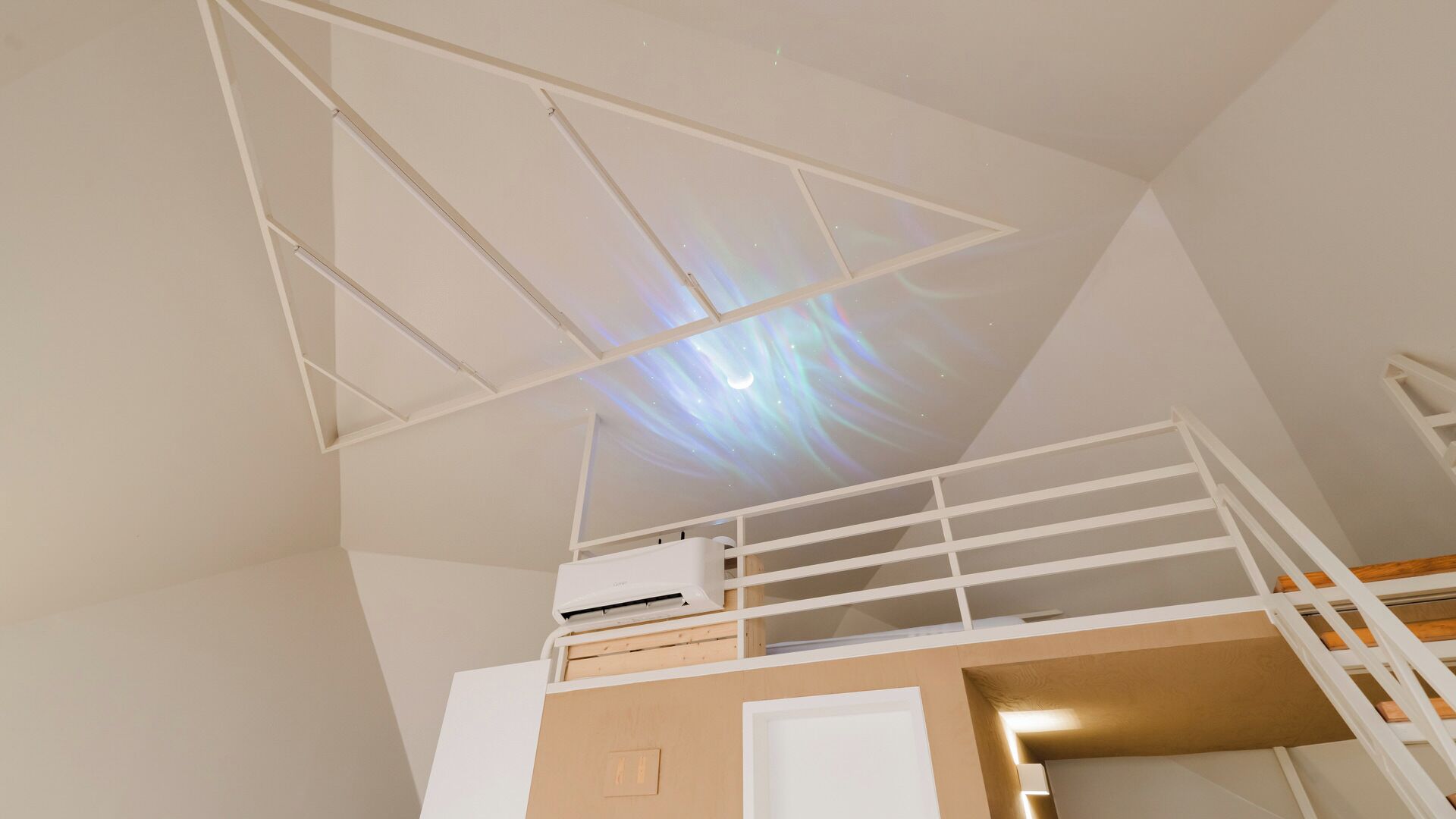 A room with a bunk bed, a ceiling projector displaying a starry sky, and a white air conditioning unit.