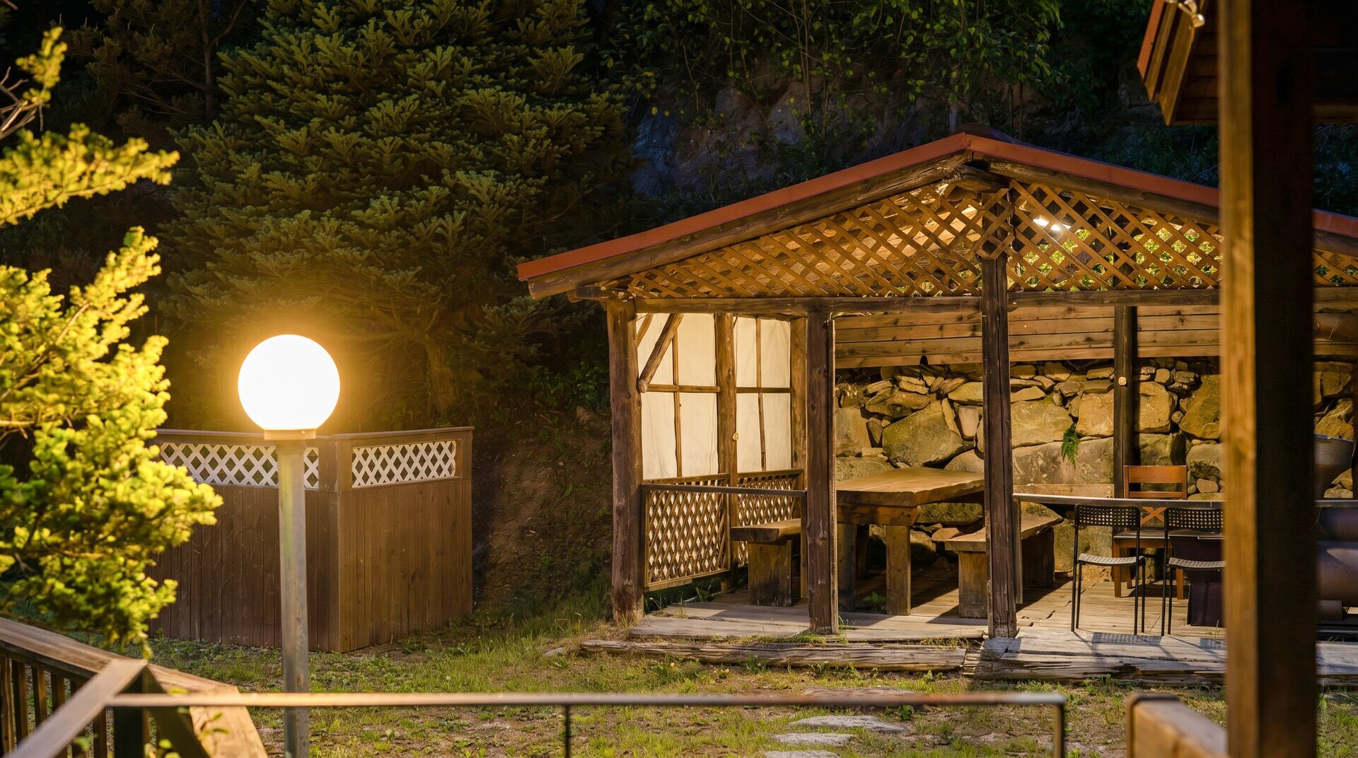 Un kiosque en bois avec un mur en pierre en arrière-plan, une table et des chaises.