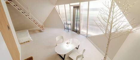A modern loft bedroom with a large window, a white dining table, and a staircase.