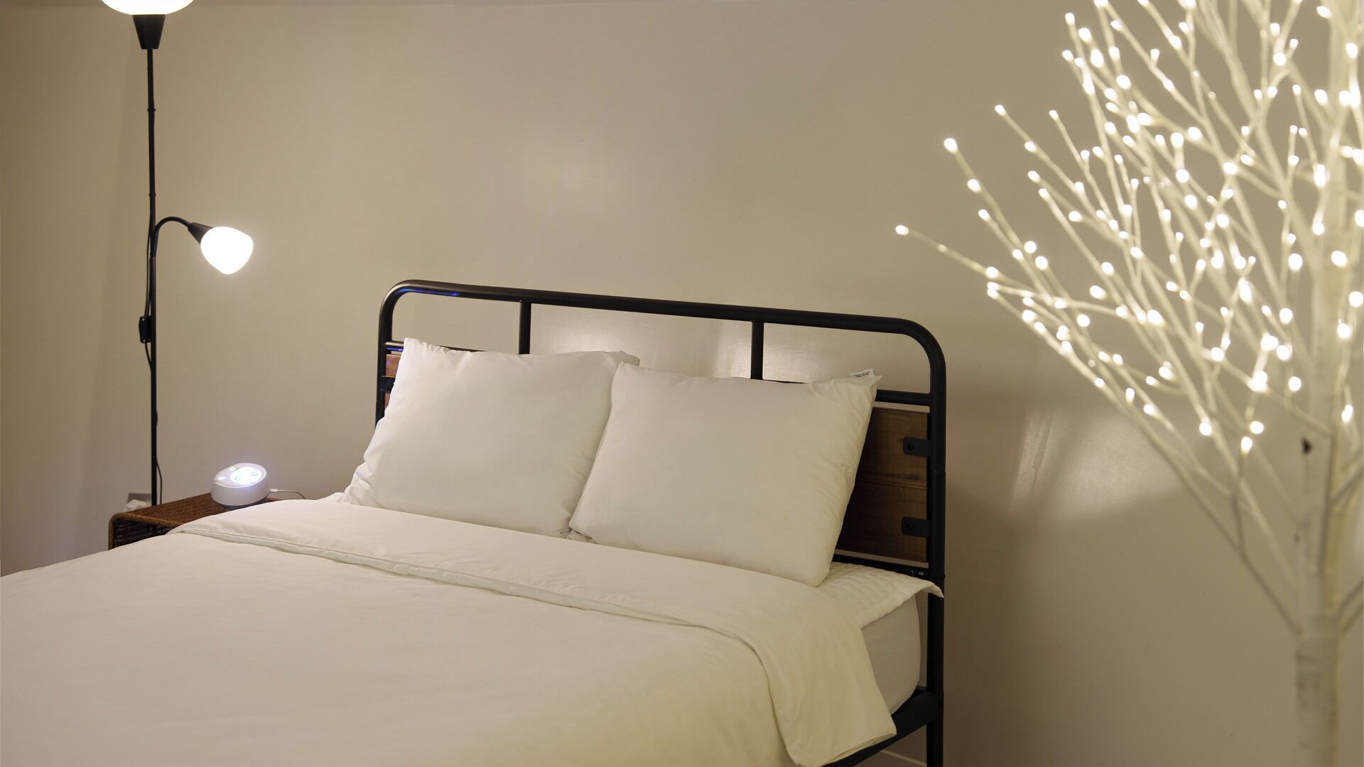 Een bed met witte beddengoed, een zwart metalen hoofdeinde, een bedlamp en een decoratieve verlichtingsarmatuur.