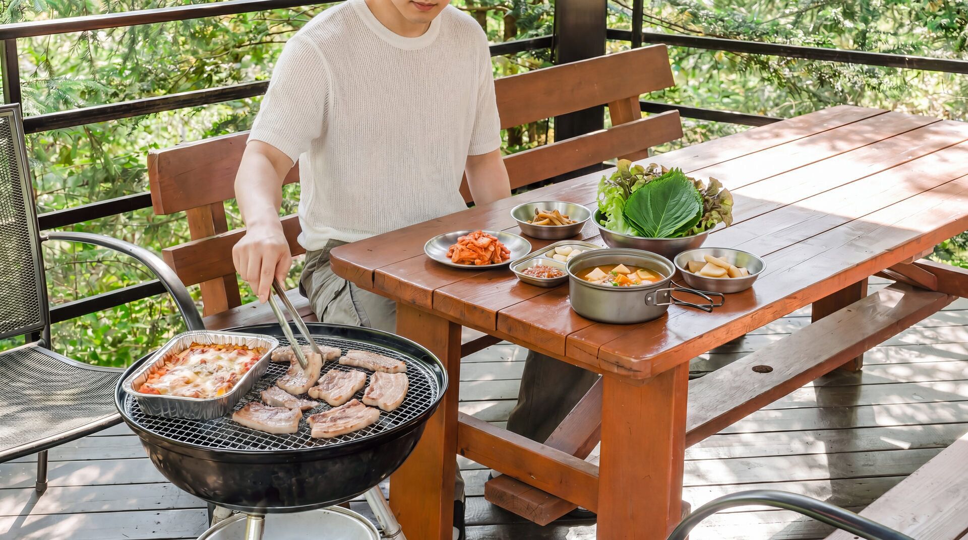A person grilling meat on an outdoor grill, with a wooden table and benches nearby.