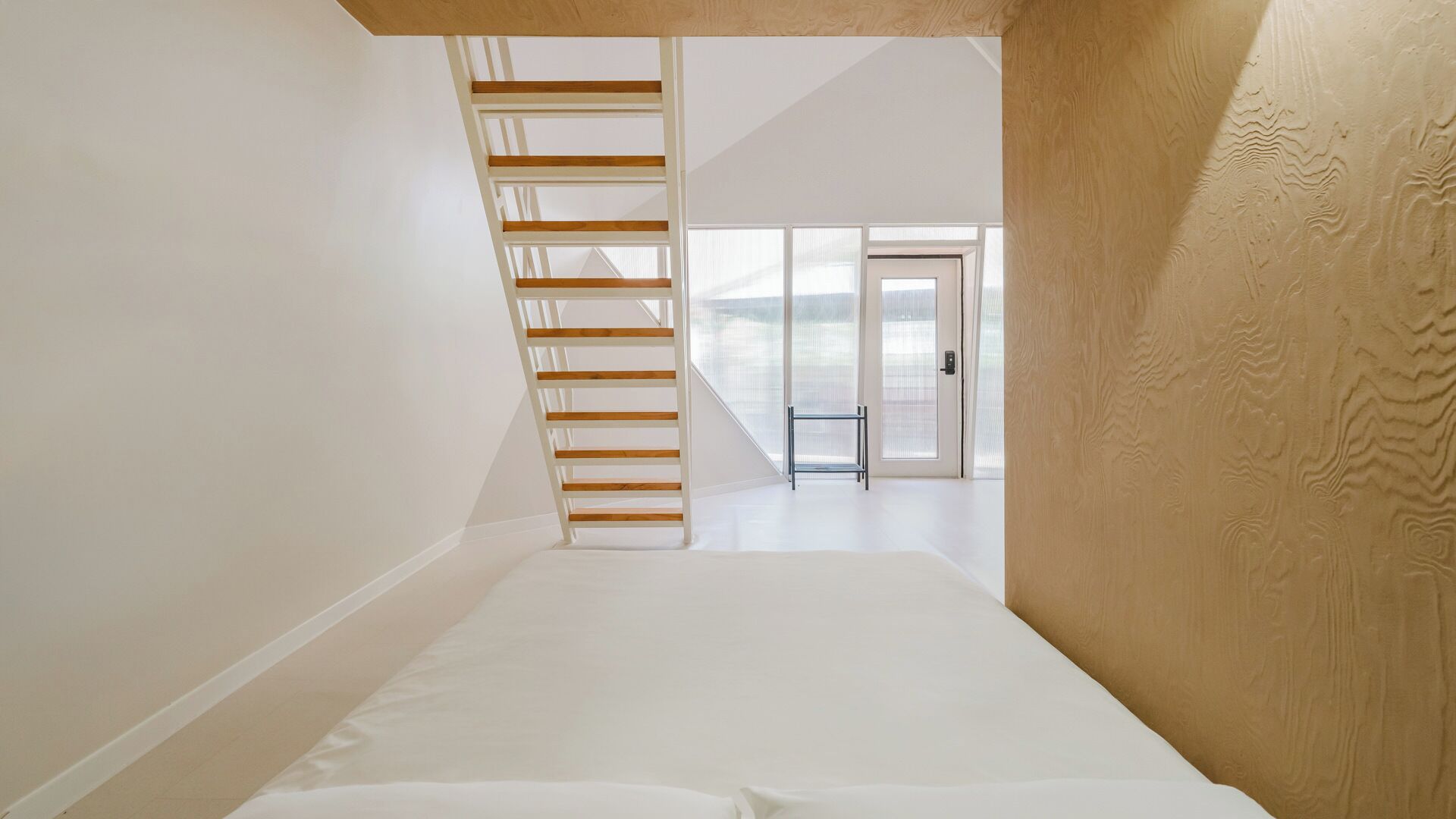 A bedroom with a wooden staircase, a large window, and a door leading to an outdoor area.
