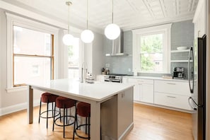 Una cocina moderna con una isla central, taburetes de bar, estufa de acero inoxidable y refrigerador.