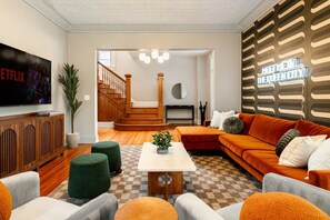 Una sala de estar con televisor, sofá, otomanas y una escalera que conduce a otra habitación.