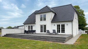 Ein zweistöckiges Haus mit einem Ziegeldach, einer Veranda mit Treppe und einer kleinen Außen-Sitzgelegenheit.