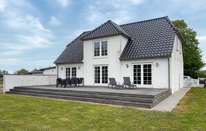 Ein zweistöckiges Haus mit einem Ziegeldach, einer Veranda mit Treppe und einer kleinen Außen-Sitzgelegenheit.