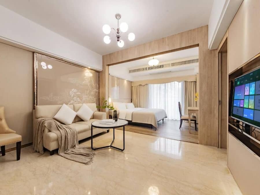 Una habitación de hotel moderna con sofá, una mesita redonda, cama y televisor en la pared.