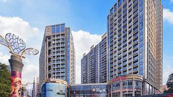 A modern urban area with high-rise buildings, a shopping center, and a prominent sculpture.