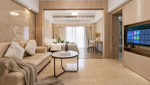 A modern hotel room with a sofa, coffee table, and a TV displaying a room service menu. - Yumi Apt Foshan Zumiao Metro Station (Foshan)