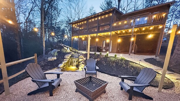 Una cabaña de madera con terraza, mobiliario exterior y un pequeño estanque.